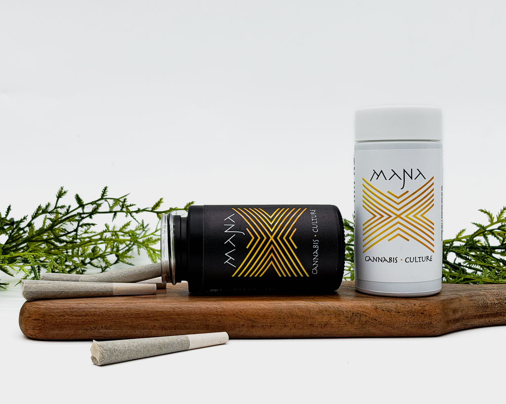 Two Mana cannabis products on a wooden board with greenery in the background