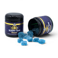 Dr. Wonderstone CBD Sleepy Time gummies in a black jar with blue sugar-coated square gummies spilled on a white surface.