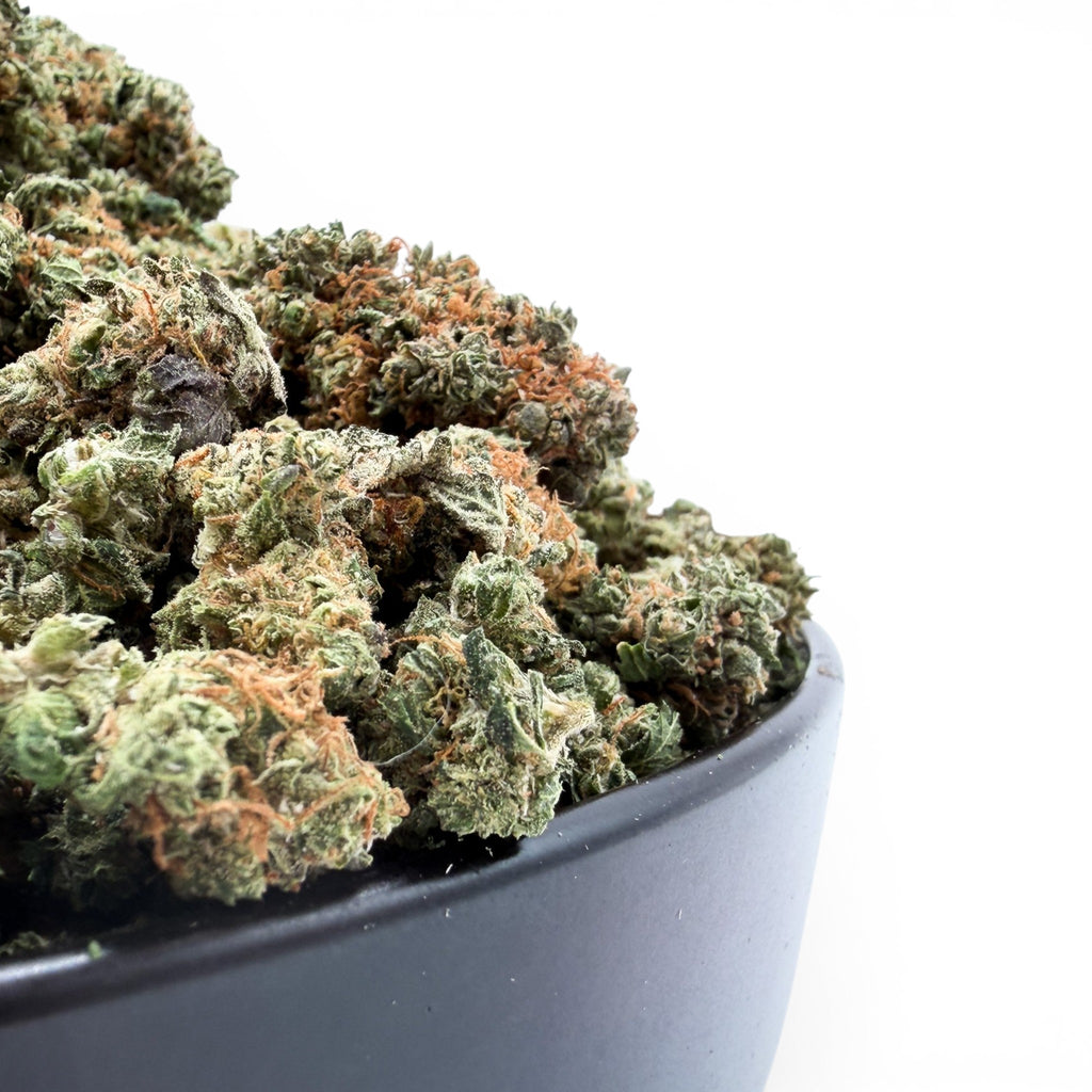 Dr. Wonderstone Pancakes premium THCa flower buds with green leaves and orange pistils in a black bowl.