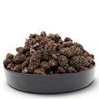 Dr. Wonderstone Tropical Cookies THCa flower in a black bowl, featuring dense, dark purple buds with visible trichomes.